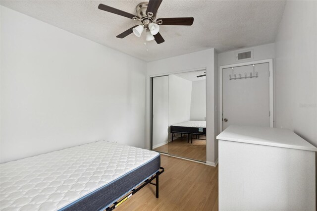 bedroom with ceiling fan, a textured ceiling, light wood-type flooring, and a closet