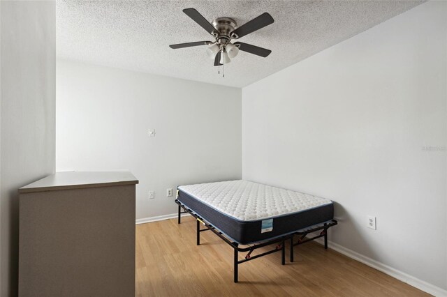 bedroom featuring light hardwood / wood-style flooring, a textured ceiling, and ceiling fan