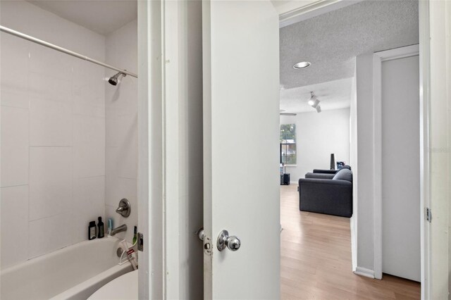 bathroom featuring a textured ceiling, hardwood / wood-style floors, and tiled shower / bath