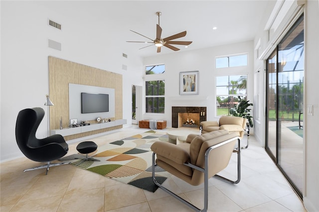 tiled living room featuring a high end fireplace, ceiling fan, and a high ceiling