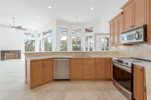 kitchen featuring appliances with stainless steel finishes, ceiling fan with notable chandelier, sink, backsplash, and kitchen peninsula