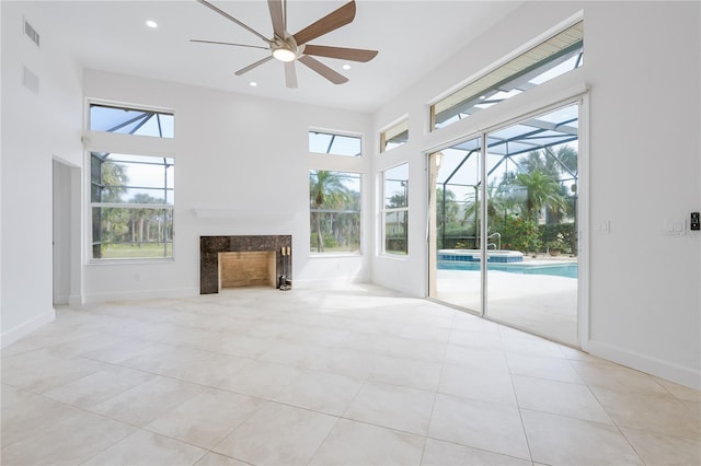 unfurnished living room featuring light tile patterned flooring, ceiling fan, a fireplace, and a high ceiling