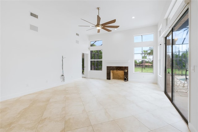 unfurnished living room with a premium fireplace, a towering ceiling, light tile patterned floors, and ceiling fan