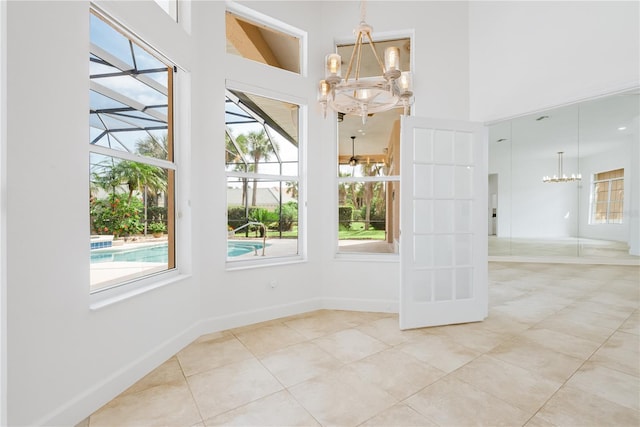 tiled spare room with a high ceiling, a notable chandelier, baseboards, and plenty of natural light