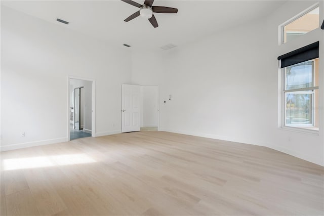 empty room with light wood-type flooring, visible vents, baseboards, and a towering ceiling