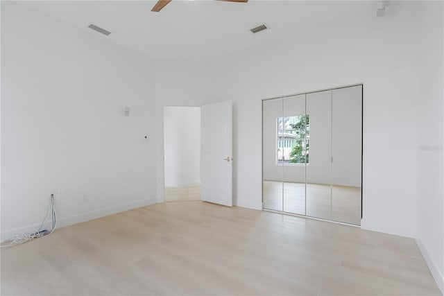 unfurnished bedroom with ceiling fan, a closet, light hardwood / wood-style flooring, and a towering ceiling