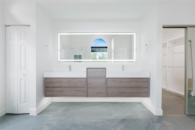 bathroom with a sink, concrete floors, double vanity, baseboards, and walk in shower