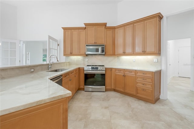 kitchen featuring a sink, backsplash, stainless steel appliances, a peninsula, and light stone countertops