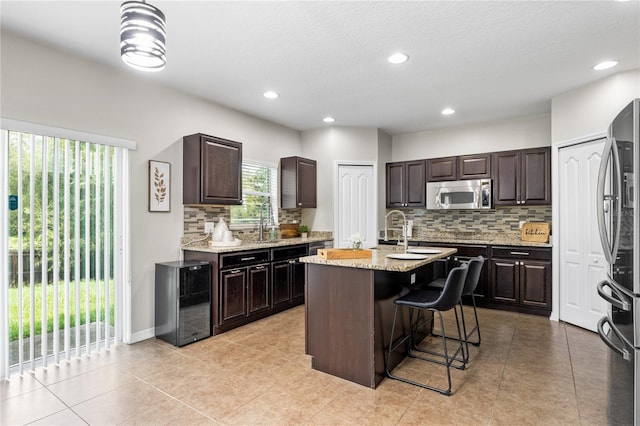 kitchen featuring decorative backsplash, appliances with stainless steel finishes, a kitchen island with sink, and light tile patterned floors