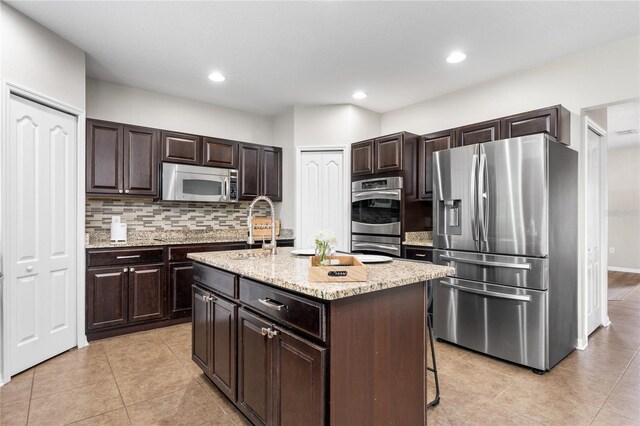 kitchen featuring decorative backsplash, a kitchen breakfast bar, light tile patterned floors, an island with sink, and stainless steel appliances