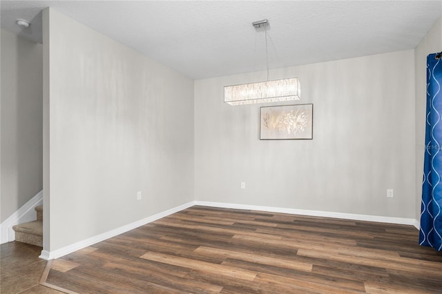 empty room with a notable chandelier, a textured ceiling, and hardwood / wood-style floors