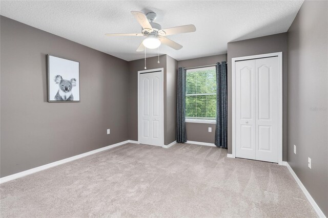 unfurnished bedroom with ceiling fan, two closets, a textured ceiling, and light colored carpet