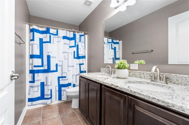 bathroom featuring a textured ceiling, dual vanity, toilet, and tile patterned floors