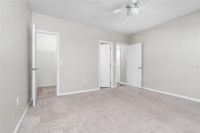 unfurnished bedroom with light carpet, a spacious closet, ceiling fan, and a closet