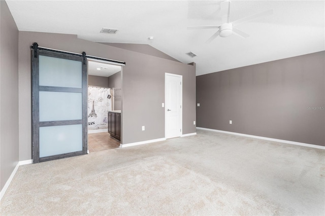 unfurnished bedroom featuring ensuite bath, carpet flooring, a barn door, and ceiling fan