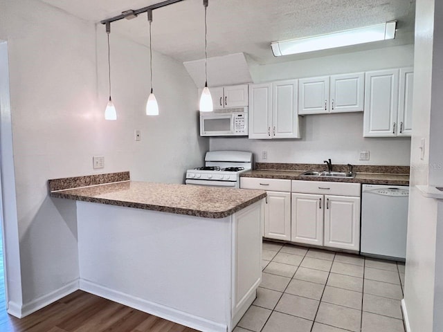 kitchen featuring white appliances, white cabinets, a sink, and a peninsula