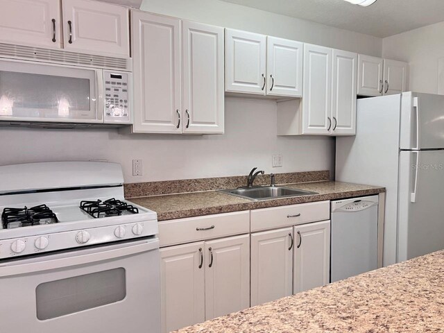 kitchen with white appliances, white cabinets, and a sink