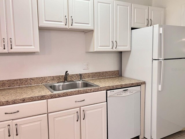 kitchen featuring white appliances, dark countertops, a sink, and white cabinetry