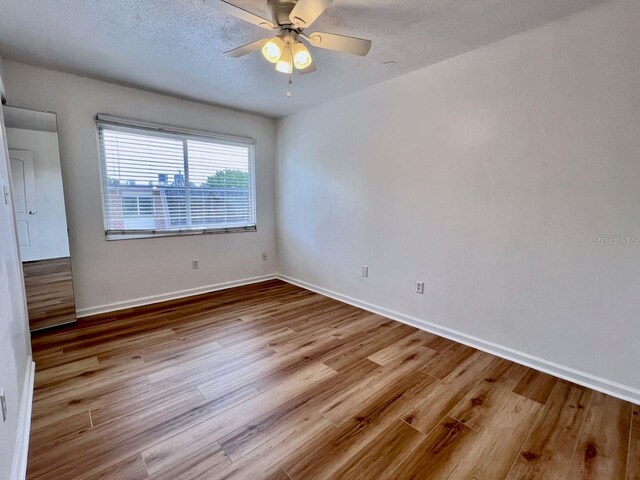 unfurnished room featuring a textured ceiling, wood finished floors, a ceiling fan, and baseboards