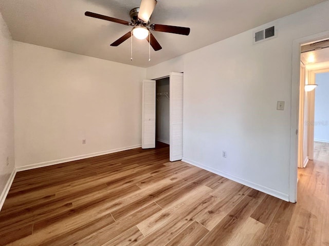 unfurnished bedroom with a closet, wood finished floors, visible vents, and baseboards