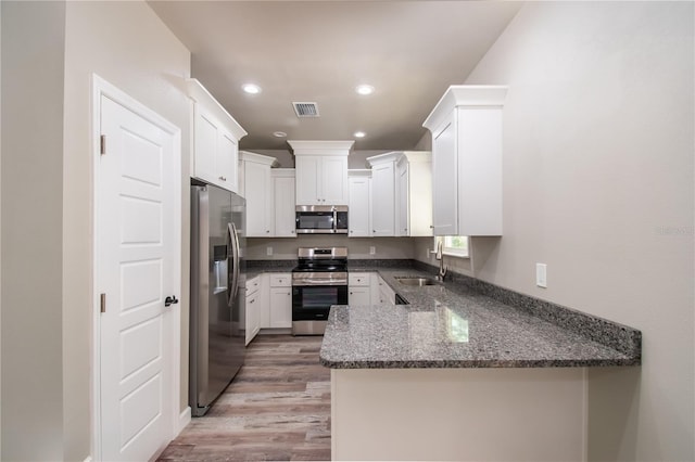 kitchen featuring stainless steel appliances, a sink, a peninsula, light wood-style floors, and recessed lighting