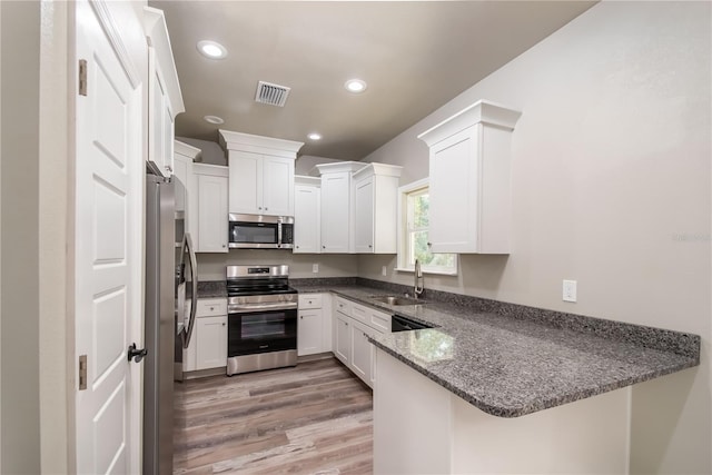 kitchen with stainless steel appliances, dark stone counters, sink, kitchen peninsula, and light hardwood / wood-style flooring