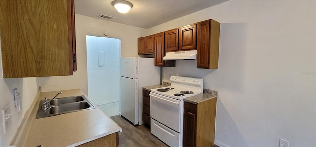 kitchen featuring white appliances, visible vents, brown cabinets, under cabinet range hood, and a sink