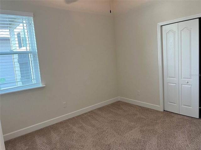 unfurnished bedroom with carpet floors, a closet, multiple windows, and baseboards