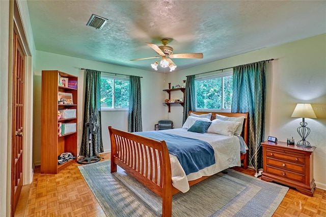 bedroom with ceiling fan, light parquet floors, and a textured ceiling