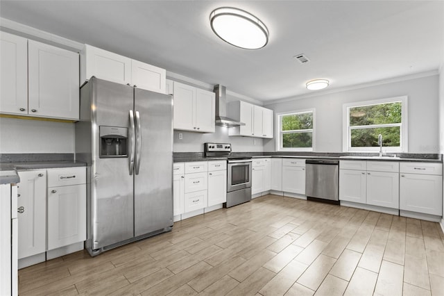 kitchen with appliances with stainless steel finishes, white cabinetry, sink, wall chimney exhaust hood, and ornamental molding