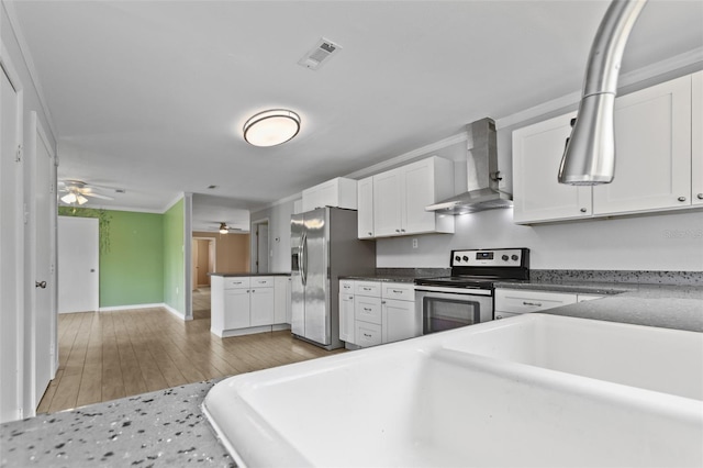 kitchen featuring white cabinetry, stainless steel appliances, ceiling fan, wall chimney exhaust hood, and light hardwood / wood-style floors