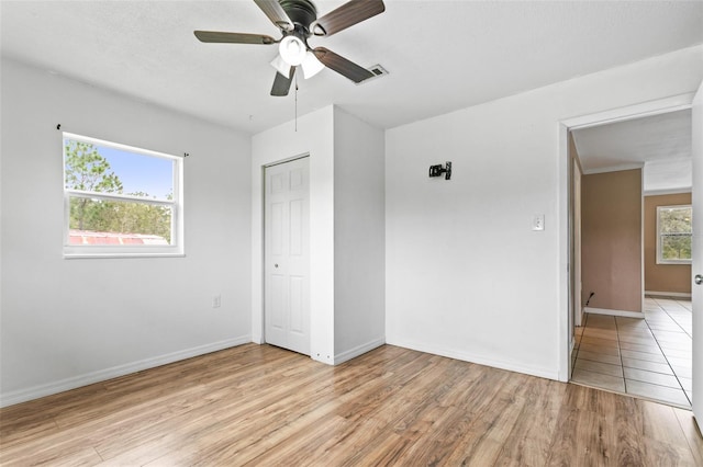 unfurnished bedroom with multiple windows, light hardwood / wood-style flooring, ceiling fan, and a closet