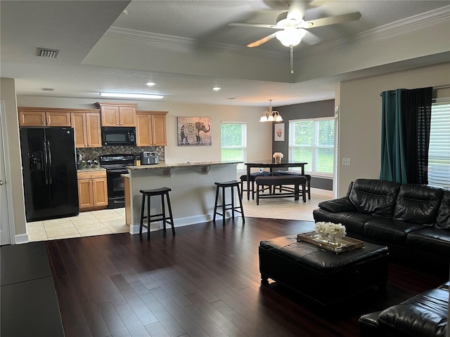 living room featuring light wood-type flooring, ceiling fan with notable chandelier, a tray ceiling, and crown molding