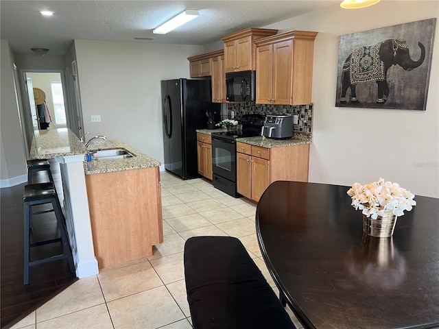 kitchen with light tile patterned flooring, sink, light stone counters, decorative backsplash, and black appliances