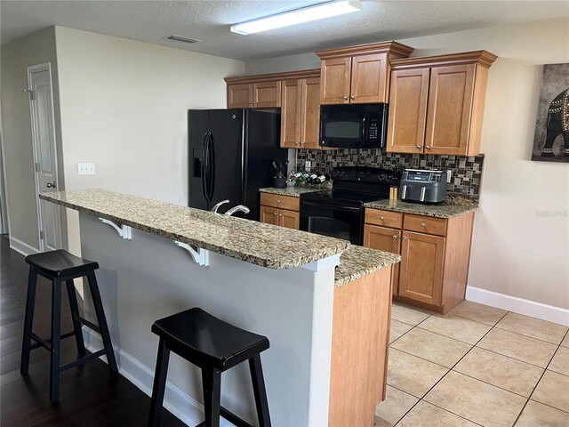 kitchen with backsplash, a breakfast bar, black appliances, a textured ceiling, and light tile patterned flooring