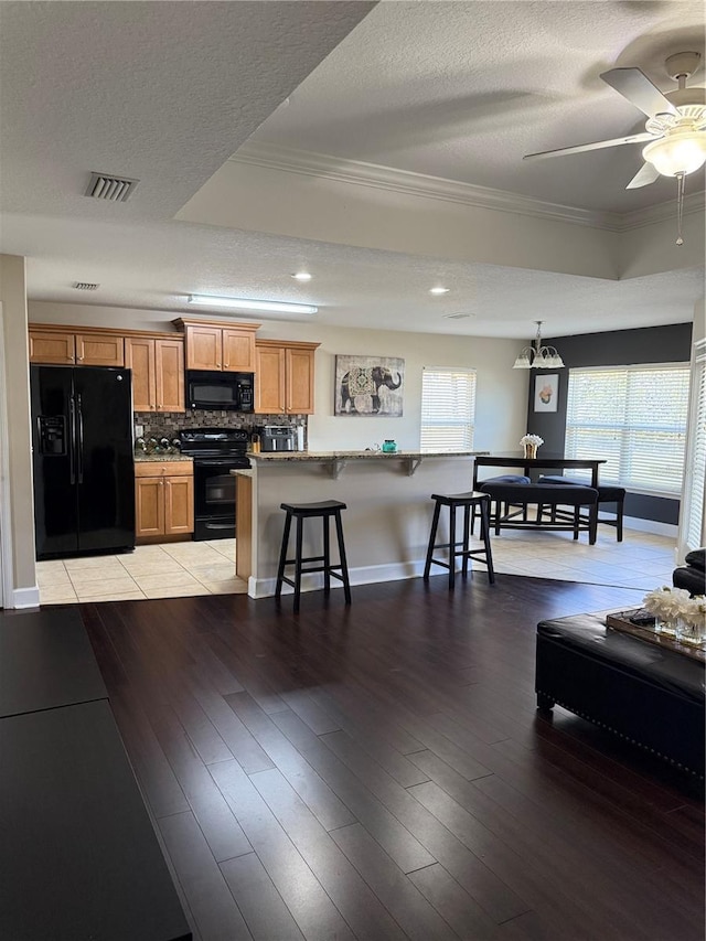 kitchen featuring black appliances, light wood-style flooring, a breakfast bar area, and crown molding