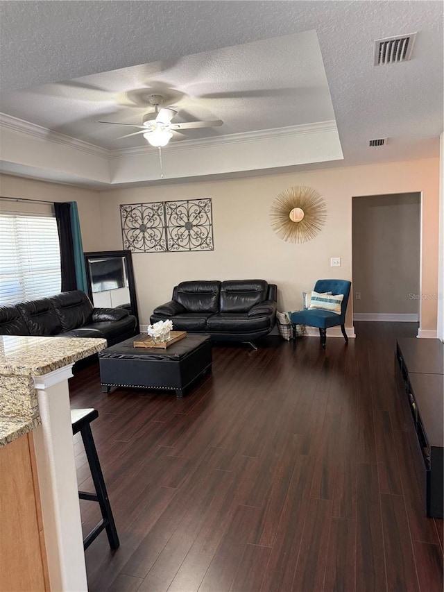 living area featuring a textured ceiling, a tray ceiling, dark wood-style flooring, and visible vents