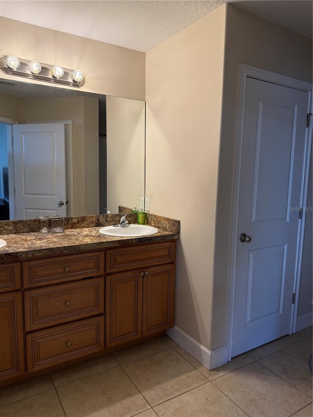 bathroom with double vanity, a sink, a textured ceiling, tile patterned flooring, and baseboards