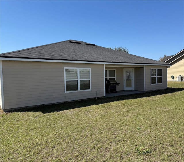 rear view of house with roof with shingles, a yard, and a patio