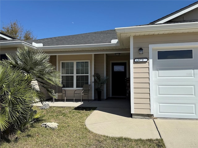 view of exterior entry with a garage, covered porch, and a shingled roof