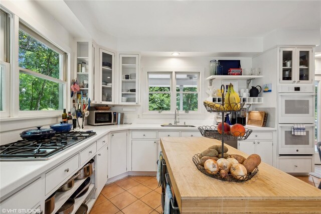 kitchen with white cabinetry, double oven, butcher block countertops, light tile patterned flooring, and sink