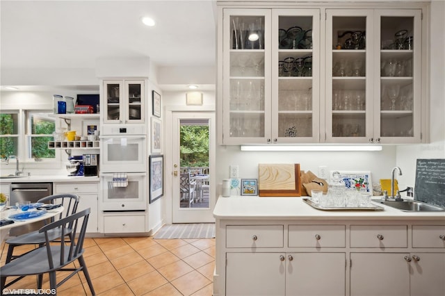 kitchen featuring sink, light tile patterned floors, white cabinets, and white double oven