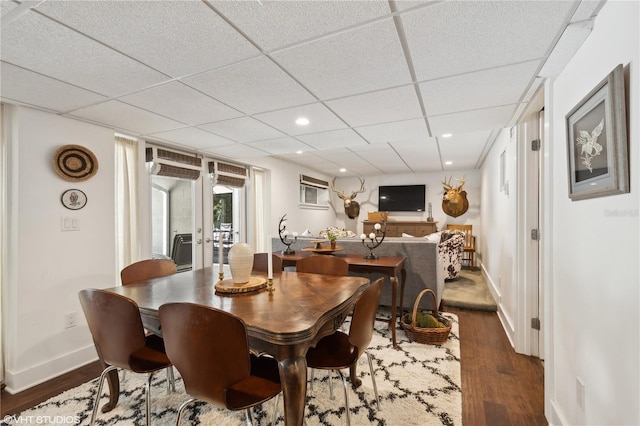 dining area with dark hardwood / wood-style floors, a wall mounted air conditioner, a drop ceiling, and french doors