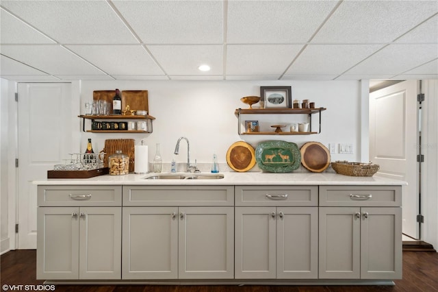 bar featuring sink, gray cabinetry, a drop ceiling, and dark hardwood / wood-style floors