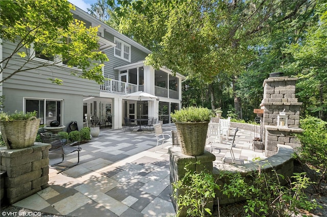 view of patio featuring an outdoor stone fireplace and a balcony