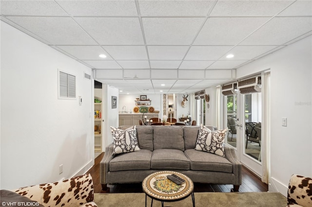 living room featuring wood-type flooring, a wall unit AC, and a paneled ceiling