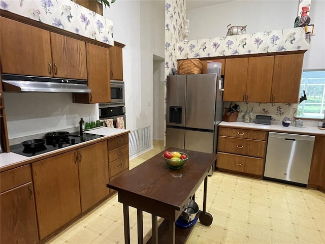 kitchen featuring light floors, stainless steel appliances, light countertops, brown cabinetry, and under cabinet range hood