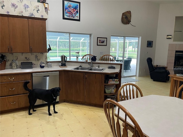 kitchen featuring a peninsula, a sink, stainless steel dishwasher, light floors, and a tiled fireplace