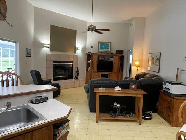 living room featuring high vaulted ceiling, ceiling fan, a tile fireplace, and sink