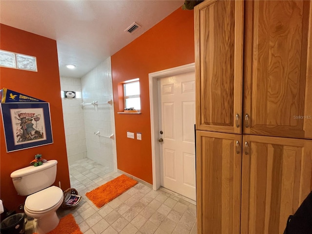 bathroom with toilet, visible vents, and tiled shower